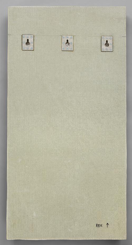 The reverse side of a panel of 18 tiles, showing the pale beige support material. There are three metal mounting pieces placed near the top of the panel. In the bottom right, “REV.” is written in black ink with a small arrow pointing upwards.