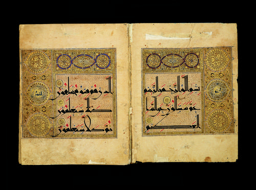 Double page spread, tan paper page with three lines of black angular text, accented by red marks, blue marks, and gold dots. Three golden medallions on the outside edge of text blocks.