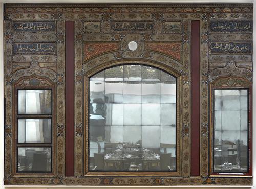 Three tall rectangular panels with cartouches filled with inscriptions and designs above three rectangular mirrors bottom of each. Each panel separated by a red rectangle. The central panel is double the width of the two on the side and has a mirror with a curved top.