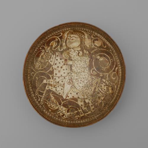View of the inside of a circular bowl, decorated in brown paint over a cream background. The bowl is painted with the image of a man riding a spotted horse, with a spotted dog running alongside. The rim is decorated with a band of arrows below a band of script.