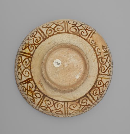 Bottom view of a circular bowl, showing the raised, unpainted base, which is smaller than the rim’s diameter. The sides are decorated with brown painted swirls over a cream background. There is a sticker with “P.30” printed on it affixed to the base.