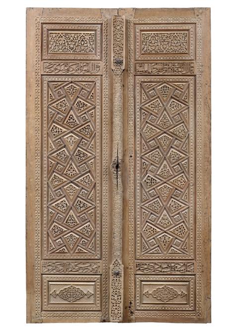 Brown wood doors, each rectangular form, the central tall vertical panel flanked above and below by smaller panels, one door with central door post to cover the join. Featuring geometric interlace design of strapwork, the polygons thus formed slightly raised and deeply carved with floral designs. 