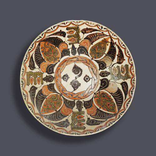 Bowl of truncated conical form, decorated in orange-red, green and dark brown slip over white with a design. Four calligraphic motifs interspersed between large palmettes formed of abstracted foliate motifs, radiating from a central medallion.