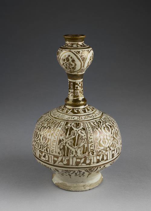 Brown and white bottle of baluster form, with bulbous body, slender ridged neck and globular mouth. The body is decorated with a large band of panels filled with foliate forms, pseudo-calligraphic bands and inscriptions around the shoulder, and foliate cartouches to neck and mouth.