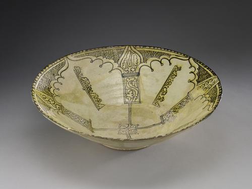 Side of dish, decorated with painting in dark brown, stained yellow, on a white slip shows. view of one arc shapes at the rim, from which an onion-shape coming from the arc has a wide bands project filled with wavy lines. Each arc is separated from the next by a line of pseudo-Kufic.