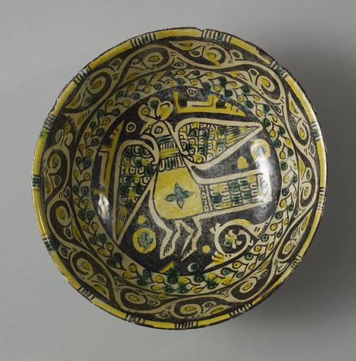 Bowl painted in yellow, purple-black and green. A large, predominantly yellow peacock,  in the centre with spots of green decoratng his tail and wings. Around the center, a band of green and yellow flowers.