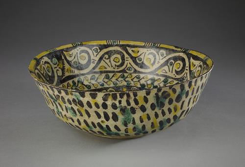 Bowl painted in yellow, purple-black and green. The sides are decorated with simple, thick, purple-black arabesques. The outside walls decorated with purple-black dashes and random spots of yellow and green.