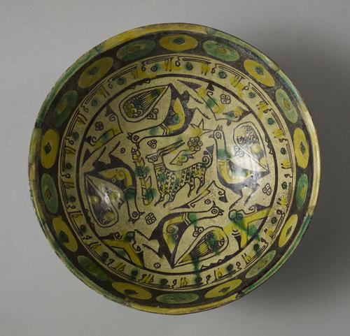 Bowl, in the centre, stands a small antelope, buff coloured and outlined in purple-black. Four yellow and purple-black peacocks circle around him. On the rim a large row of yellow and green circles on a purple-black ground. 