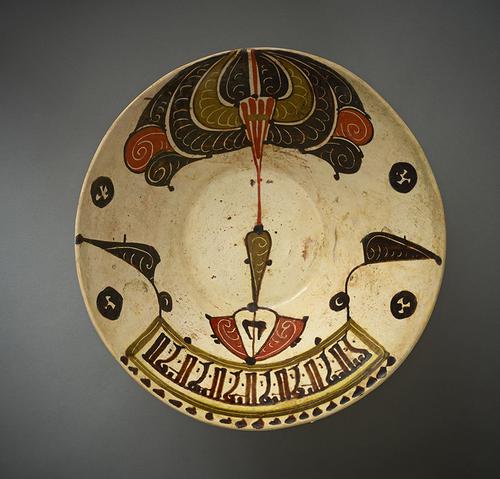 Bowl, with deep everted sides, the interior decorated on one side with a stylized peacock motif and a band of angular cursive kufic script on the other, painted in olive-green, manganese-brown, tomato-red against a cream ground.