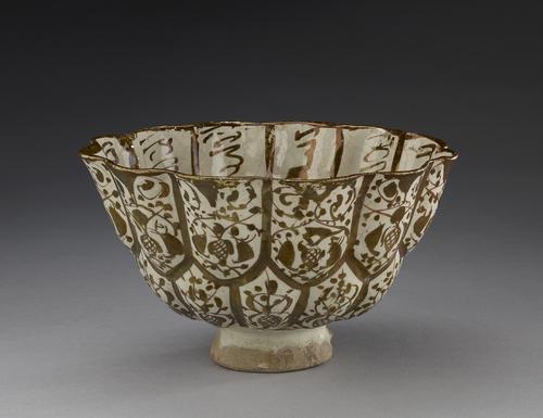 Bowl with high hollow foot supports a lower and upper zone, each consisting of twelve lobes decorated in brown lustre. The exterior lobes in both zones are filled with arabesque designs.