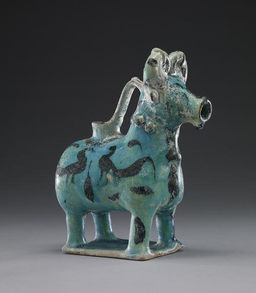 Turquoise-blue vessel in teh shape of a Bull, decorated with two black birds, presumably peacocks, decorate each side of the body. A hole in the middle of its back is joined to its head by a handle while the snout opens into a spout.