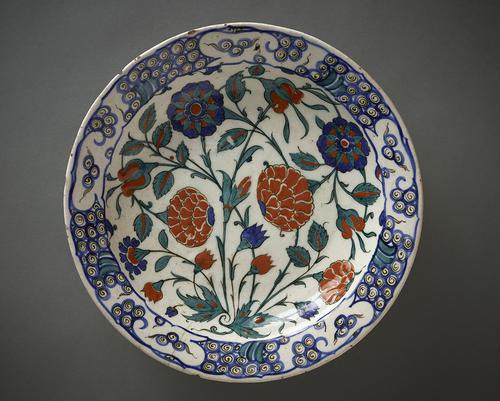 Ceramic dish, with slightly concave sides, the interior decorated with roses and buds, painted in cobalt-blue, emerald-green sealing-wax red and black against an opaque-white ground.