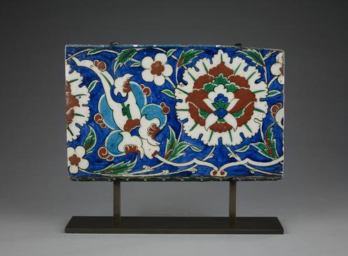 Ceramic tile, rectangular form, decorated with a large open artichoke design, blossoms and leaves, painted in turquoise and cobalt-blue, emerald-green, tomato-red, black and white, on a black mount.   