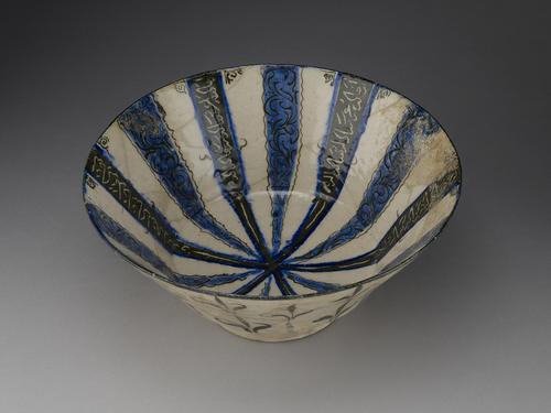 White bowl decorated in blue and black. Twelve stripes radiate from the centre of the bowl: six are blue with black borders and black waterweed decoration, the other six are black with blue borders and white inscriptions. The side walls are decorated with black waterweeds.