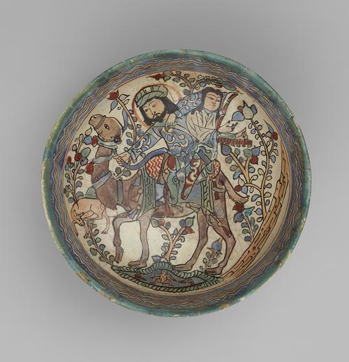 Ceramic bowl decorated with a colourful hunting scene. Man on camel aims arrow at a deer while woman on back of camel plays a harp. 