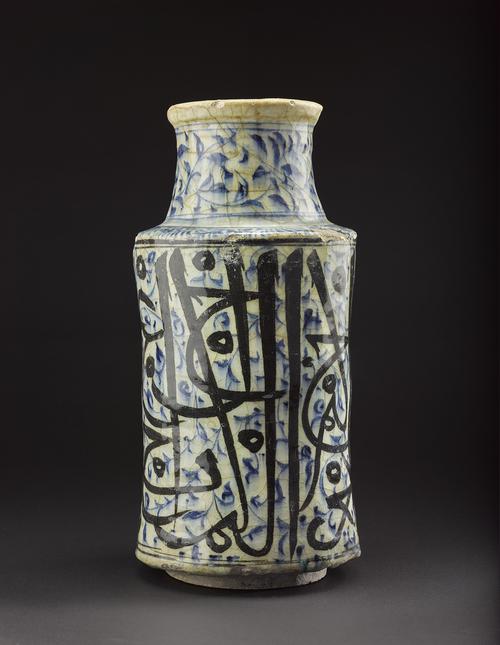 Albarello of waisted cylindrical form, decorated in underglaze cobalt blue and black with a bold calligraphic design against floral scrolls and dots. 
