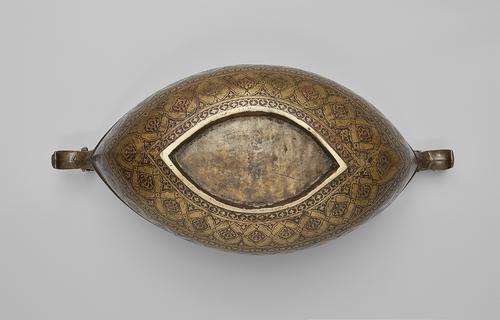 Underside of a narrow brass bowl. Base is a pointed oval. The bowl is heavily engraved, with bands of florals motifs. The underside of two dragon heads on the pointed rim are visible.